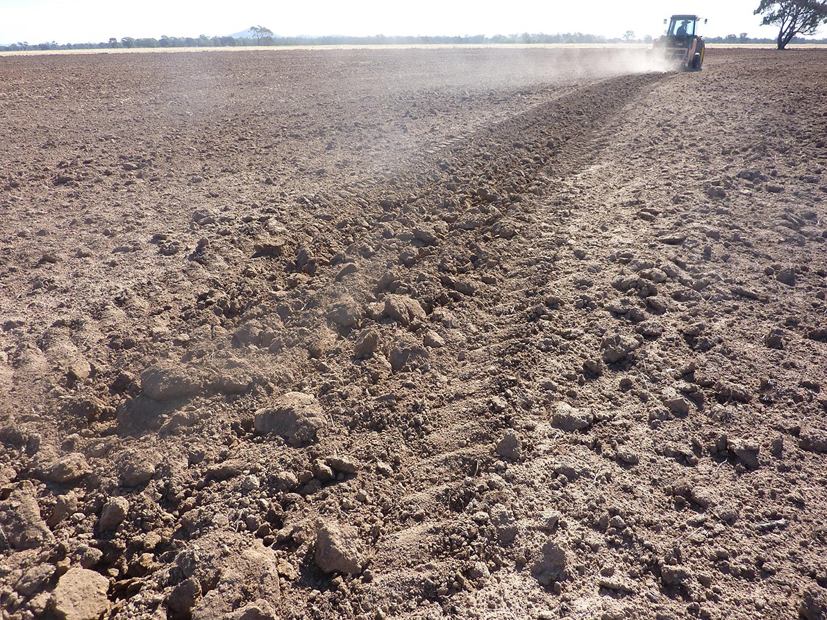 A dirt paddock with a tractor in the background.