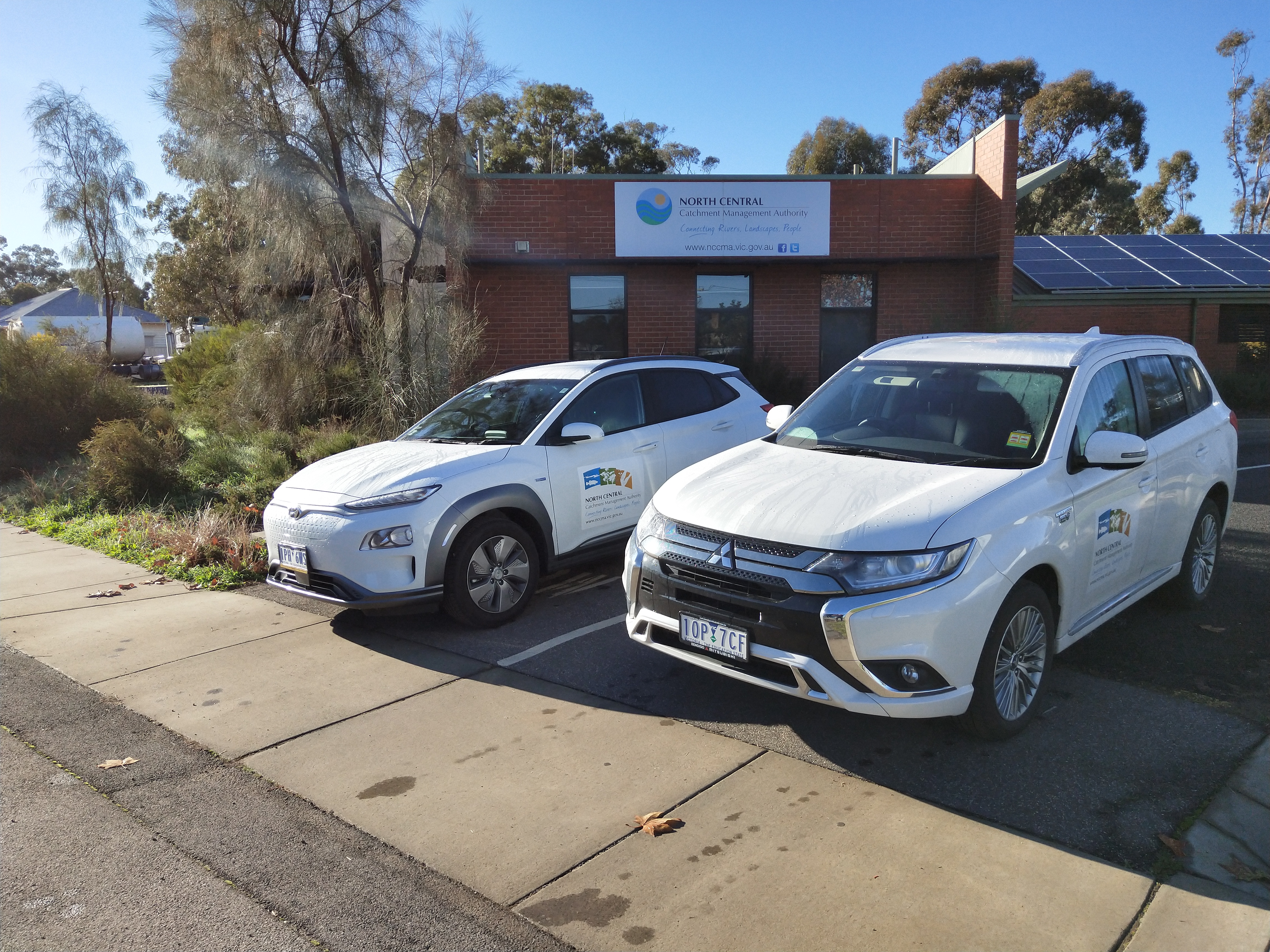 Two electric cars in a driveway of an office blocks, with solar panels in the background